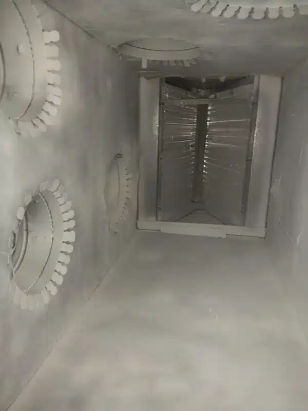 Interior view of a residential ductwork system under construction, showing white flexible ducts connected to ceiling-mounted vents and a central return air plenum or junction box. The unfinished drywall and exposed framing indicate this is during the building or renovation phase of HVAC installation. Multiple duct openings with collar fittings are visible along the ceiling structure.