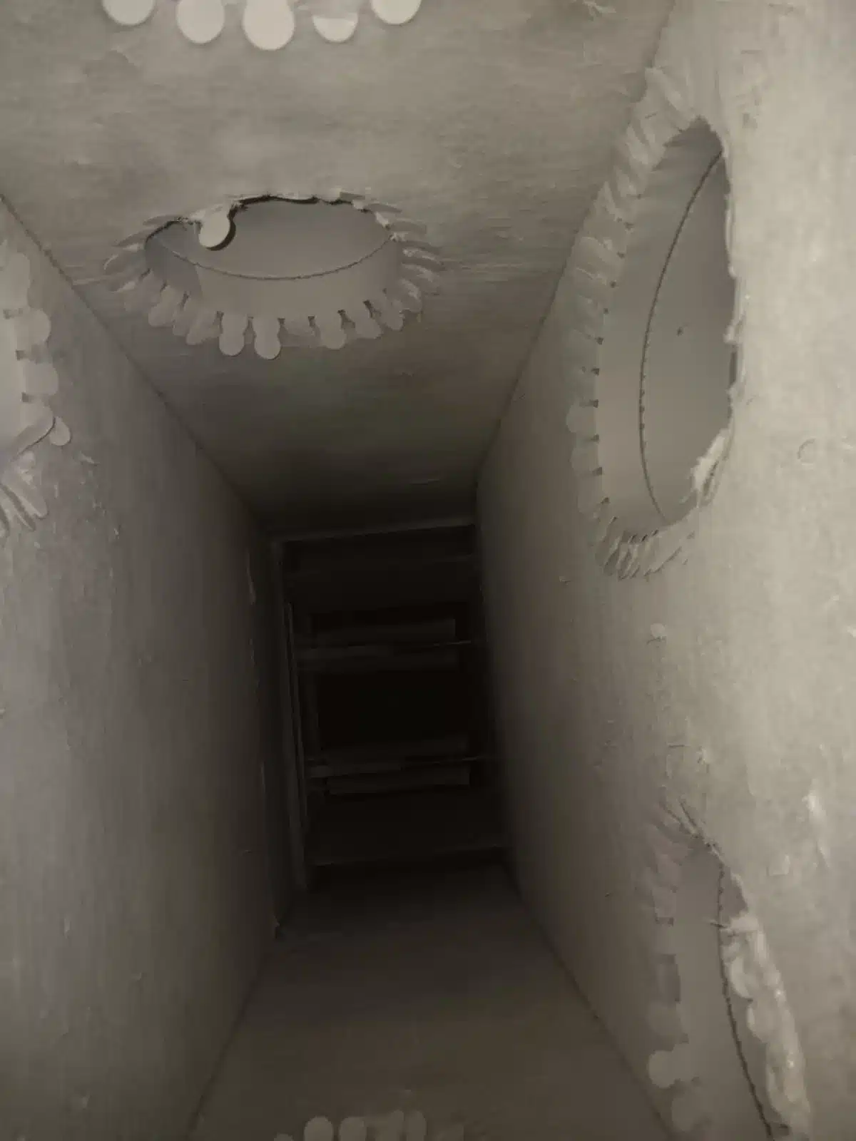 Interior of a rectangular duct cavity with light-colored surfaces, circular side openings and a dark far end.